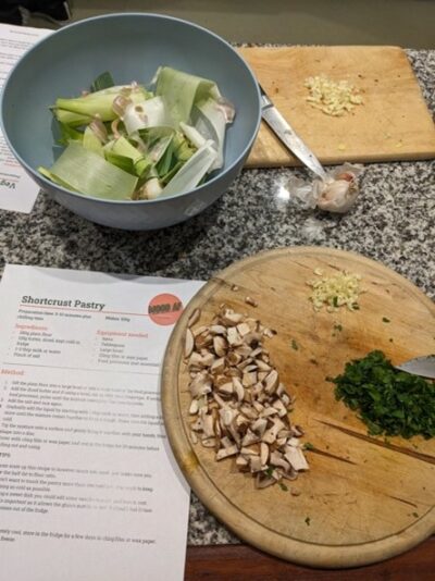 Photo shows a written recipe for shortcrust pastry next to a board with some chopped vegetables on it.