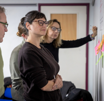 Image shows a group of people looking at post-it notes on the wall. The post-it notes contain ideas and thoughts written down by the participants of the Food Matters facilitated session.